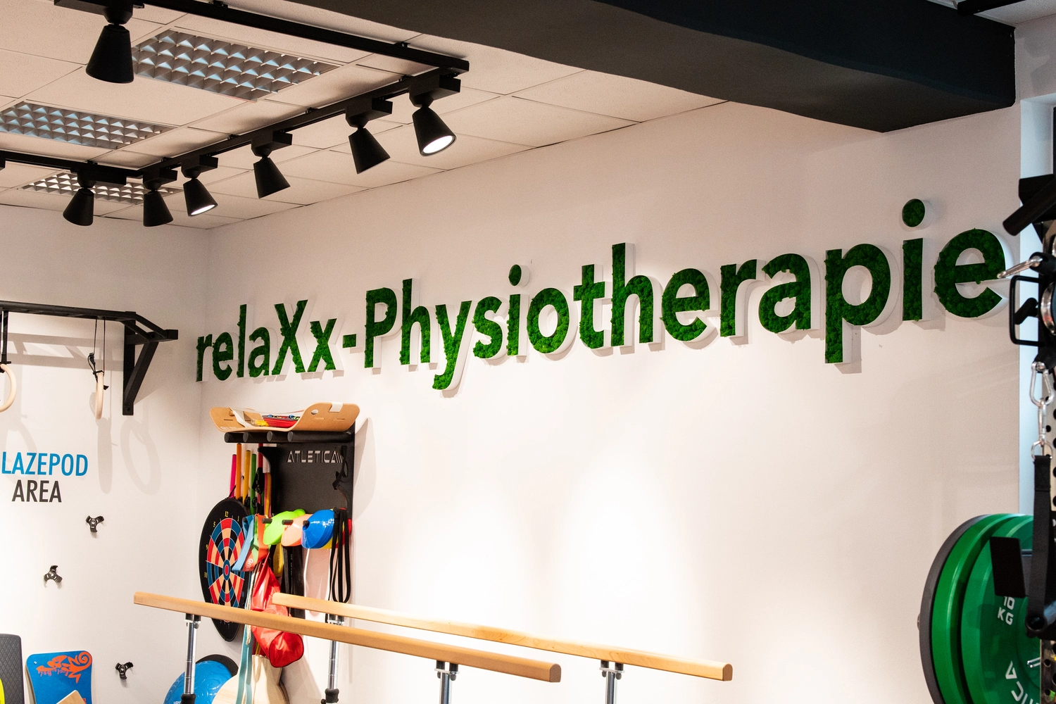 Relaxx Physiotherapie - Praxis for Physiotherapie - Das Logo von Relaxx Physiotherapie befindet sich an einer Wand des Raumes, und weitere Therapiegeräte hängen an der Wand.