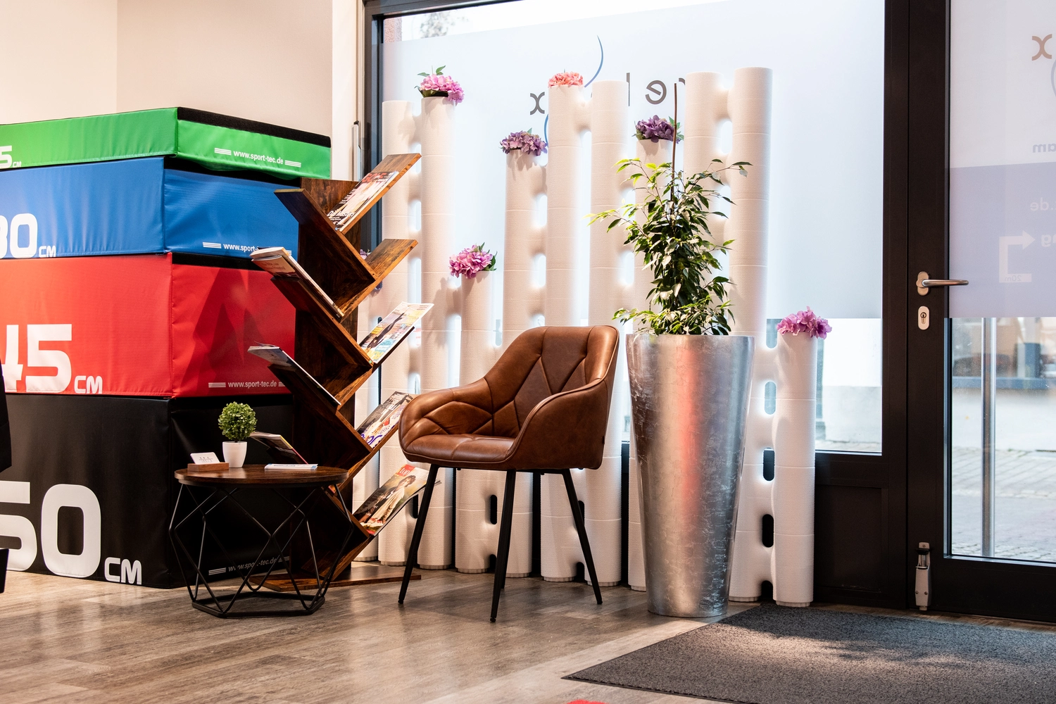 Relaxx Physiotherapie - Praxis for Physiotherapie - Ein Stuhl und ein Holzregal in einem Zimmer mit Blumenvasen hinter dem Stuhl